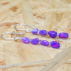 May include: A pair of silver dangle earrings with purple iridescent gemstone beads. The earrings have a simple hook closure.
