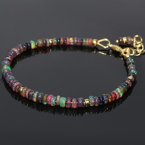 May include: A delicate bracelet made with a strand of colourful opal beads and gold accents. The bracelet has a gold clasp.