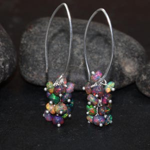 May include: A pair of silver hoop earrings with a cluster of iridescent opal gemstones dangling from each hoop.
