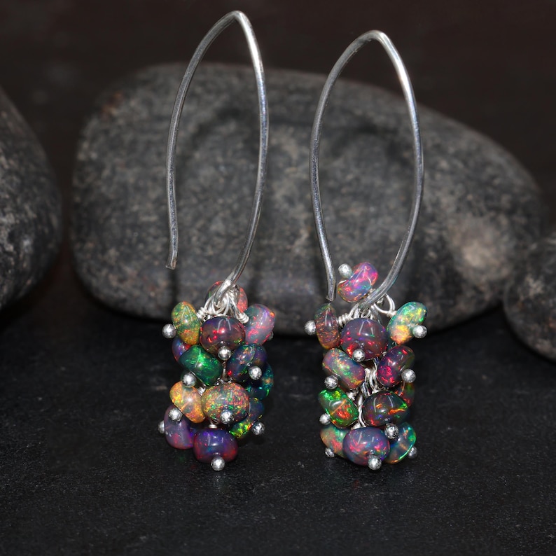 May include: A pair of silver hoop earrings with a cluster of iridescent opal gemstones dangling from each hoop.