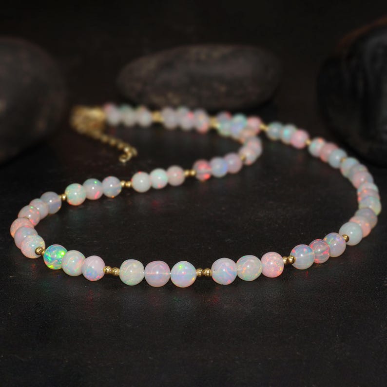 May include: A delicate necklace made of white opal beads with a subtle iridescent shimmer. The beads are separated by small gold spacers, creating a classic and elegant look.