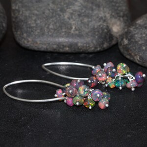 May include: A pair of silver dangle earrings with a cluster of iridescent opal beads. The beads are various shades of pink, purple, and black.