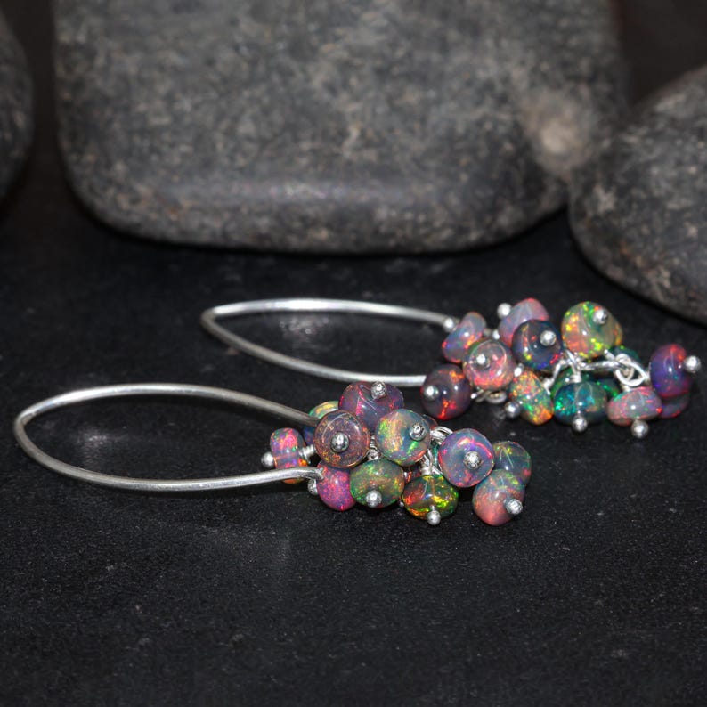 May include: A pair of silver dangle earrings with a cluster of iridescent opal beads. The beads are various shades of pink, purple, and black.