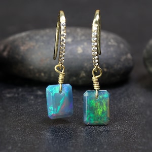 May include: A pair of gold earrings with a rectangular opal gemstone dangling from each earring. The earrings have a diamond-encrusted wire that leads to a gold wire wrapped around the opal.