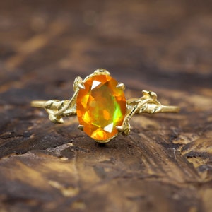 May include: A gold ring featuring a large oval orange opal gemstone set in a delicate, twig-like design.
