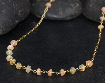 May include: A delicate gold chain necklace with small, round, iridescent opal beads. The necklace is on a black background.