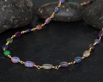 Può includere: Una delicata collana con opali ovali nei toni del blu, viola e verde, infilati con una catena color oro. Gli opali hanno una qualità scintillante e iridescente. La collana è esposta su una superficie scura.