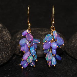 Könnte beinhalten: Ein Paar goldfarbene Ohrringe mit Trauben aus ovalen Opalen in Lila- und Blautönen. Jedes Opal ist mit kleinen goldenen Perlen verziert. Die Ohrringe hängen an goldfarbenen Haken.