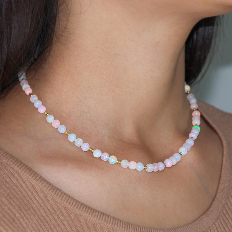 May include: A delicate necklace with small, iridescent opal beads and gold accents. The necklace is made of a thin chain and has a simple, elegant design.