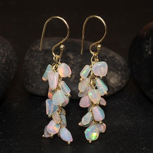 May include: A pair of gold dangle earrings with a cluster of iridescent white opal stones. The earrings are approximately 2 inches long.