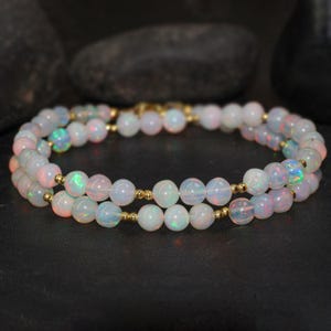 May include: A double strand necklace made of white opal beads with gold spacers. The necklace is on a dark background.