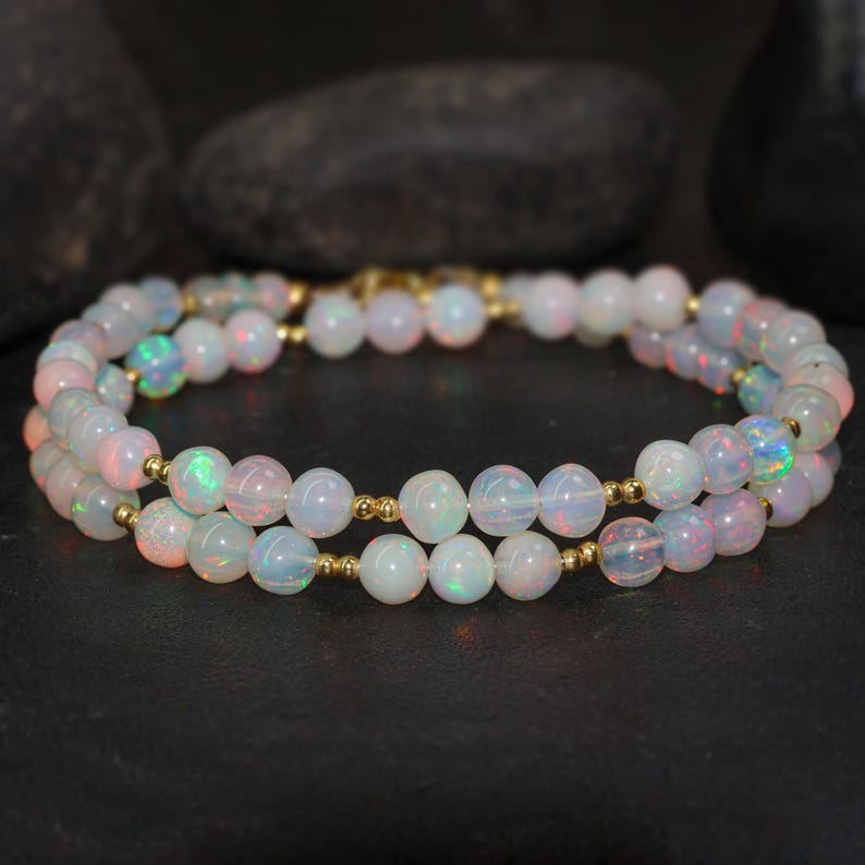 May include: A double strand necklace made of white opal beads with gold spacers. The necklace is on a dark background.