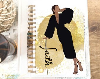 Könnte beinhalten: Ein weißes Spiralnotizbuch mit goldenem Hintergrund und einer Schwarzweißillustration einer Frau in einem schwarzen Kleid. Das Wort "Glaube" ist in goldener Schrift auf dem Cover geschrieben.