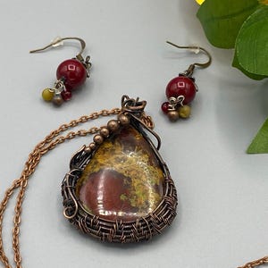May include: A copper wire wrapped pendant necklace with a red and yellow stone, and matching earrings with red beads.