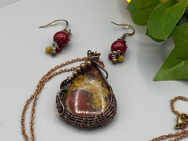 May include: A copper wire wrapped pendant necklace with a red and yellow stone, and matching earrings with red beads.