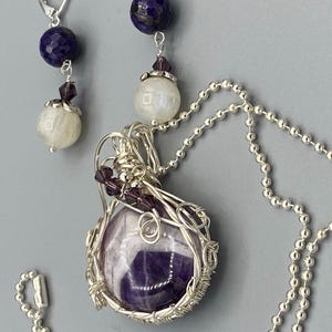 May include: A silver chain necklace with a wire-wrapped amethyst pendant and a silver chain with a pair of earrings featuring a blue stone and a white stone.