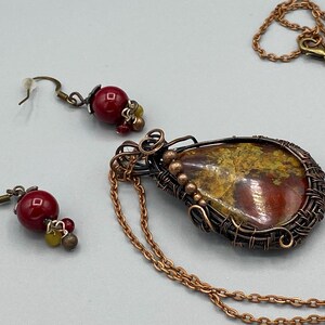 May include: A copper wire wrapped pendant necklace with a red and yellow agate stone. The necklace comes with matching earrings with red glass beads.