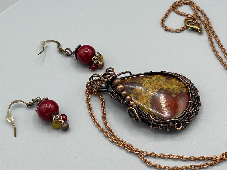 May include: A copper wire wrapped pendant necklace with a red and yellow agate stone. The necklace comes with matching earrings with red glass beads.
