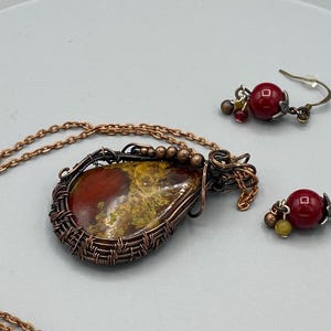 May include: A copper wire wrapped pendant necklace with a red and green agate stone and matching earrings with red glass beads.