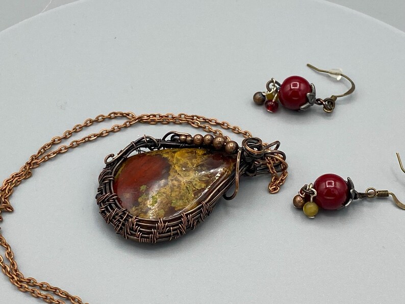 May include: A copper wire wrapped pendant necklace with a red and green agate stone and matching earrings with red glass beads.