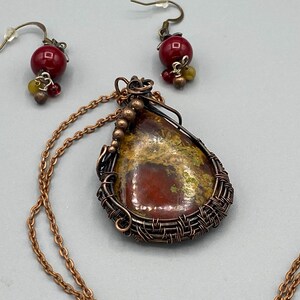May include: A copper wire wrapped pendant necklace with a red and yellow agate stone. The necklace has a matching pair of earrings with red and yellow glass beads.