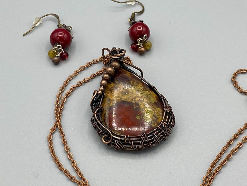 May include: A copper wire wrapped pendant necklace with a red and yellow agate stone. The necklace has a matching pair of earrings with red and yellow glass beads.