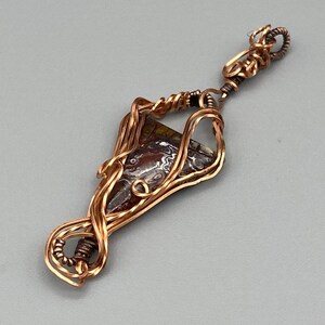 May include: A copper wire wrapped pendant featuring a brown, green, and white agate stone.