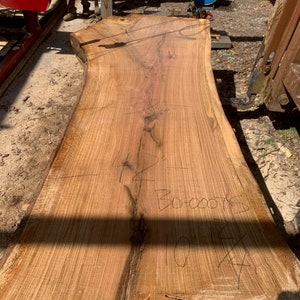 May include: A large slab of wood with a natural wood grain pattern. The wood is light brown in color and has a few knots. The wood is marked with the text "BO-00015" and "10' x 4'" in black marker.