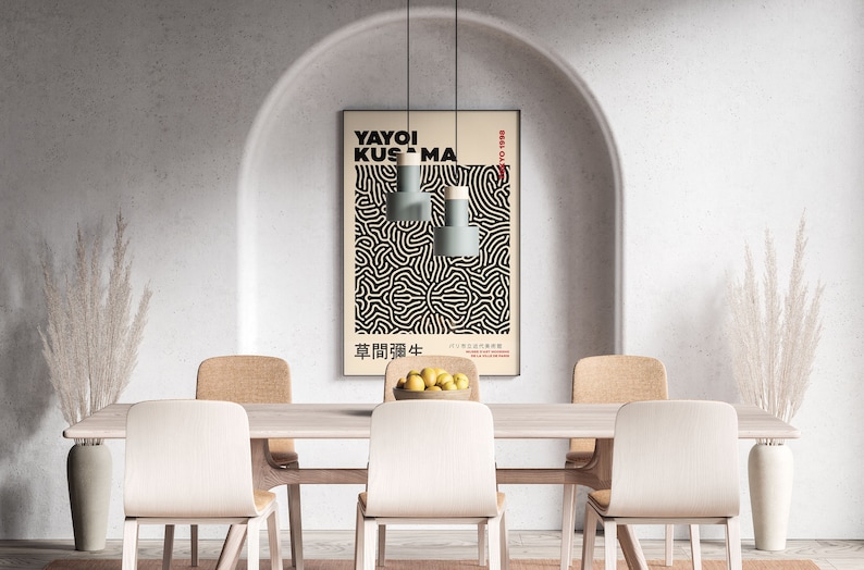 May include: A dining room with a white wall and an arched doorway. A poster with black and white abstract art hangs on the wall. The poster features the text "YAYOI KUSAMA" and Japanese characters. There are four chairs and a table with a bowl of lemons in the center.