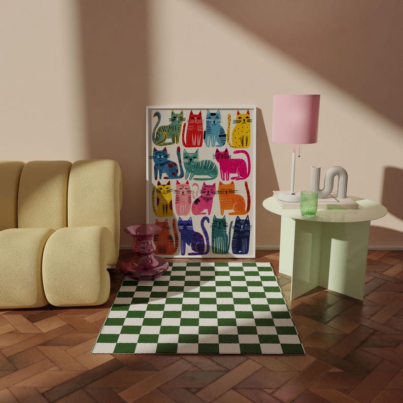 K&ouml;nnte beinhalten: Zimmer mit einem gerahmten Katzenkunstdruck, einem gelben Sofa, einer rosa Lampe und einem gr&uuml;n-wei&szlig; karierten Teppich. Der Kunstdruck zeigt farbenfrohe Katzenillustrationen. Ein kleiner, runder, hellgr&uuml;ner Tisch tr&auml;gt ein gr&uuml;nes Glas und eine wei&szlig;e Skulptur.