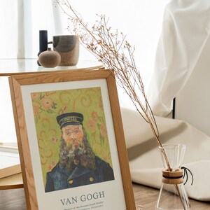 May include: A framed print of a painting by Vincent van Gogh titled "Portrait of the Postman Joseph Roulin". The painting depicts a man with a beard wearing a blue uniform and a black cap. The background is a green and yellow floral pattern.