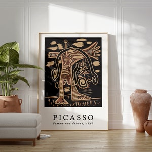 May include: A framed poster with a black background and a gold abstract figure. The poster has the text "PICASSO" and "Femme nue debout, 1963" printed below the image.