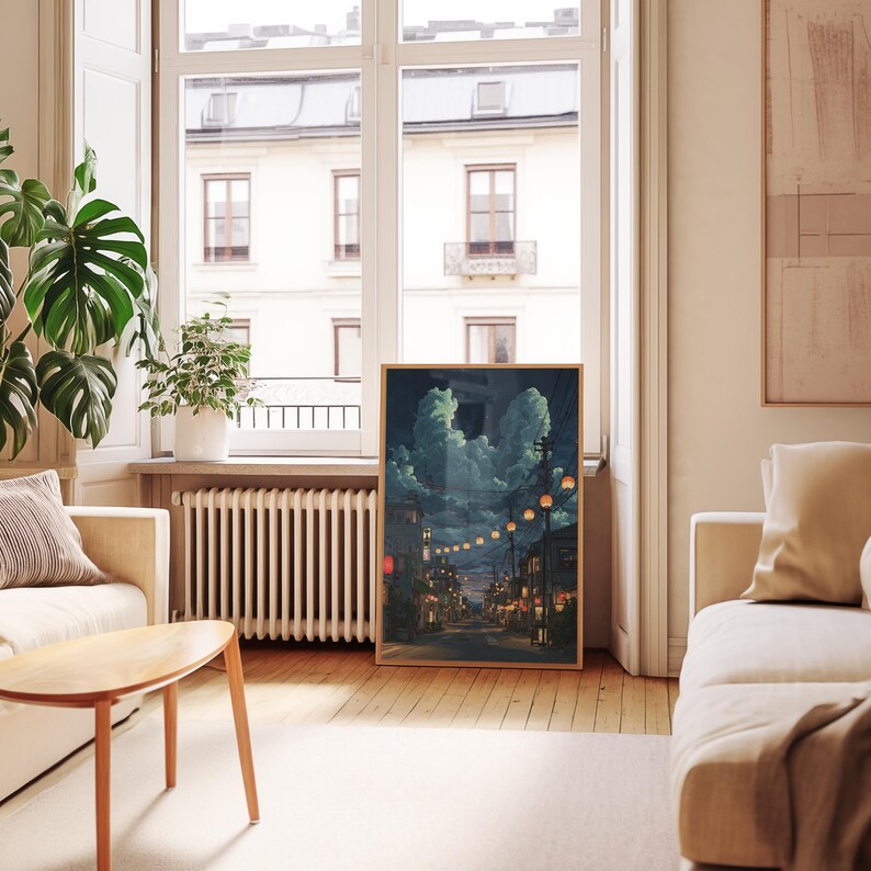 May include: A framed art print depicts a nighttime street scene with glowing lanterns and buildings. The artwork features a palette of blues, greens, and warm orange hues, creating a serene and atmospheric ambiance. The print is displayed in a light-colored wooden frame.