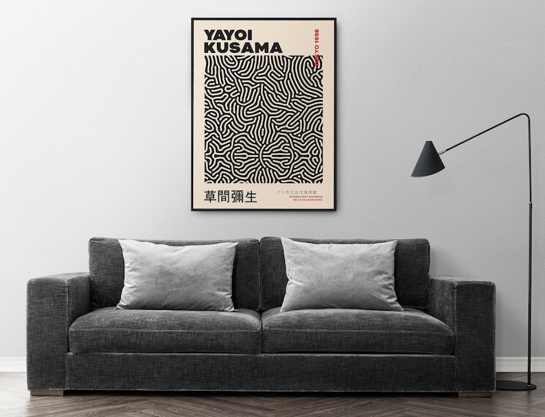 May include: A black and white poster with a geometric pattern and the text "YAYOI KUSAMA 1929-2018" and "草間彌生" in Japanese. The poster is framed and hanging on a white wall.