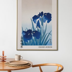 May include: A framed print of a Japanese painting featuring blue irises with green leaves. The artist's signature is in the bottom right corner, and the title "春艸界" is in the bottom left corner. The artist's name "OHARA KOSON" is printed below the signature.