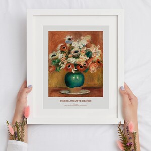 Op de afbeelding: Een ingelijste print van een schilderij van Pierre Auguste Renoir met de titel "Bloemen". Het schilderij toont een boeket rode, witte en roze bloemen in een groene vaas op een wit bord. De achtergrond is warm oranje.