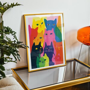 May include: A framed art print featuring a colorful illustration of multiple cats. The cats are depicted in various vibrant colors, including yellow, blue, pink, and green. The artwork is displayed in a gold frame, adding a touch of elegance.