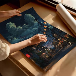 May include: A print of a nighttime street scene with glowing lanterns and buildings. The artwork features a dark blue sky with fluffy clouds. The print is being held on a wooden surface.