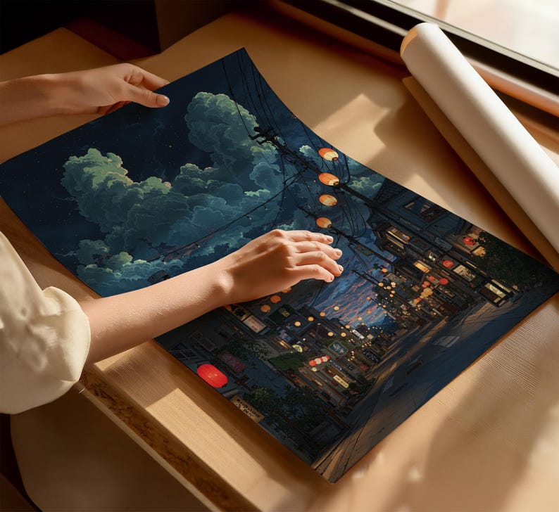 May include: A print of a nighttime street scene with glowing lanterns and buildings. The artwork features a dark blue sky with fluffy clouds. The print is being held on a wooden surface.