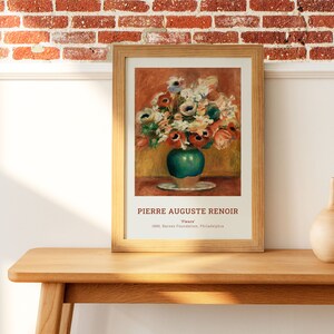 Op de afbeelding: Een ingelijste print van een schilderij van Pierre Auguste Renoir met de titel "Bloemen". Het schilderij toont een boeket kleurrijke bloemen in een groene vaas op een wit bord. Het schilderij is ingelijst in een lichtbruin houten lijst.