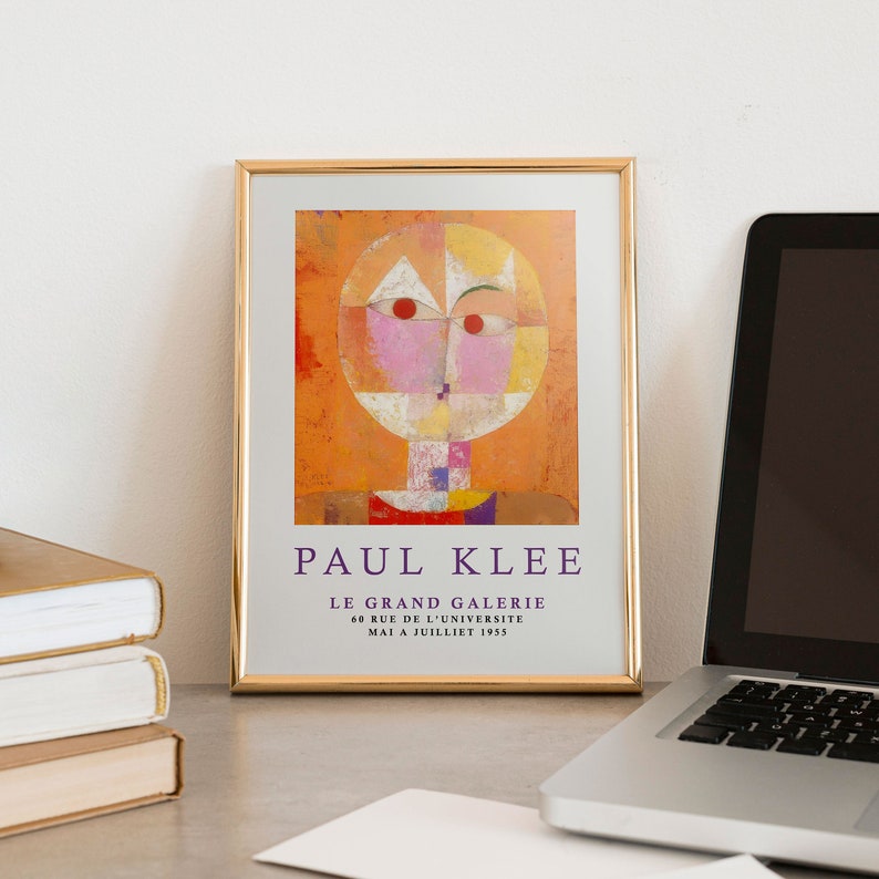 May include: A framed poster featuring an abstract painting by Paul Klee. The painting depicts a stylized human face with geometric shapes in shades of orange, yellow, pink, and red. The poster includes the text "PAUL KLEE", "LE GRAND GALERIE", "60 RUE DE L'UNIVERSITE", and "MAI A JUILLET 1955".