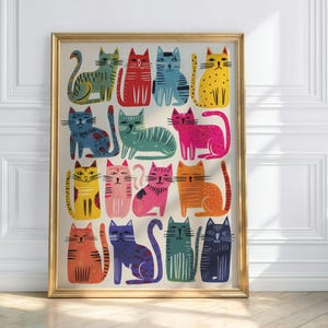 K&ouml;nnte beinhalten: Ein gerahmter Kunstdruck mit einer Sammlung farbenfroher, stilisierter Katzenillustrationen. Die Katzen sind in verschiedenen Posen und Farben dargestellt, darunter Rot, Blau, Gelb und Pink, vor einem cremefarbenen Hintergrund. Der Rahmen ist goldfarben.
