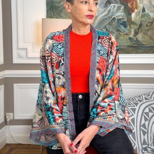 Peut inclure: Une femme portant un kimono à motifs colorés avec un haut rouge et un jean noir. Le kimono a un motif géométrique avec des nuances de bleu, rouge, orange et blanc.