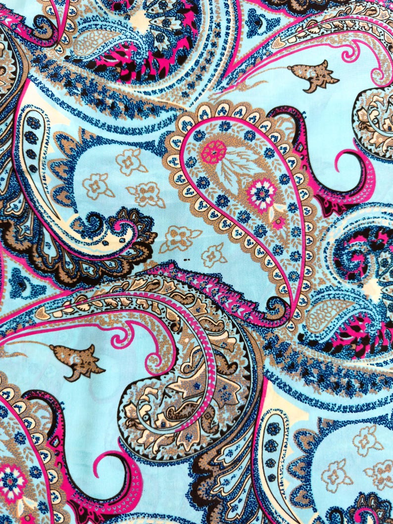 May include: A close-up of a fabric with a paisley pattern. The design features large, swirling paisley shapes in shades of blue, pink, brown, and white against a light blue background. The pattern is detailed and intricate, with a mix of solid and dotted lines.