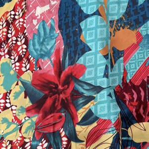 May include: A colourful fabric with a floral pattern. The fabric features red, pink, blue, yellow and green flowers and leaves. The fabric has a geometric pattern in the background.