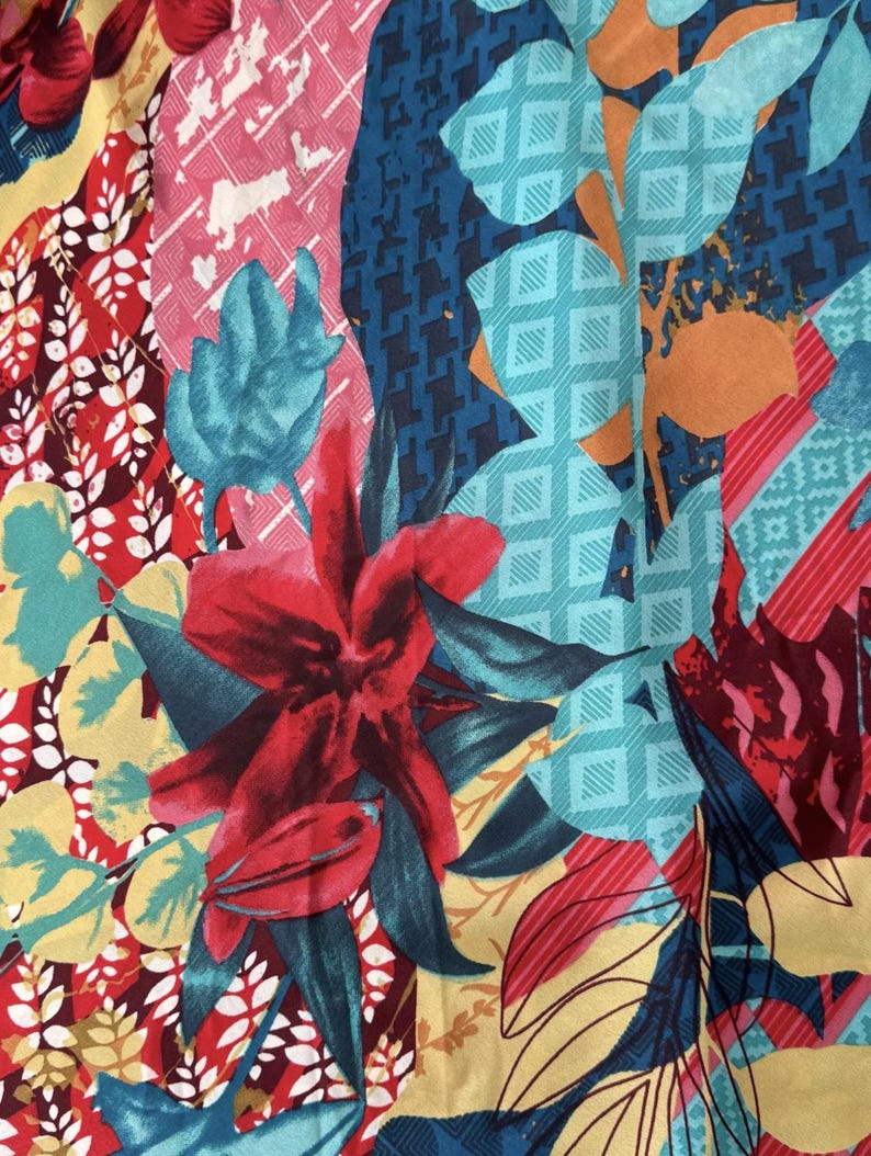 May include: A colourful fabric with a floral pattern. The fabric features red, pink, blue, yellow and green flowers and leaves. The fabric has a geometric pattern in the background.