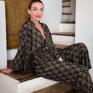 May include: A woman wearing a black and gold patterned jumpsuit with a V-neckline. The jumpsuit has a geometric design with a subtle sheen.