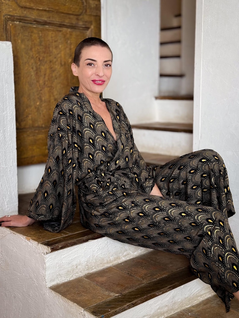 May include: A woman wearing a black and gold patterned jumpsuit with a V-neckline. The jumpsuit has a geometric design with a subtle sheen.
