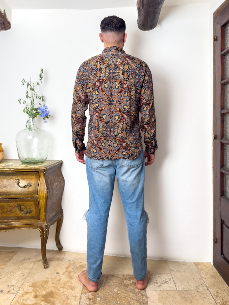 May include: A man wearing a long-sleeved shirt with a colorful paisley pattern and blue jeans.