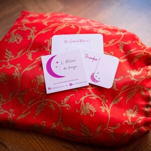 Peut inclure: Une pochette en tissu rouge avec des broderies florales dor&eacute;es et une carte blanche avec le texte "Un Grand Merci!" et une carte blanche avec le texte "Merci!" et une carte de visite avec le texte "L'Atelier de Sonja" et une adresse de site web.
